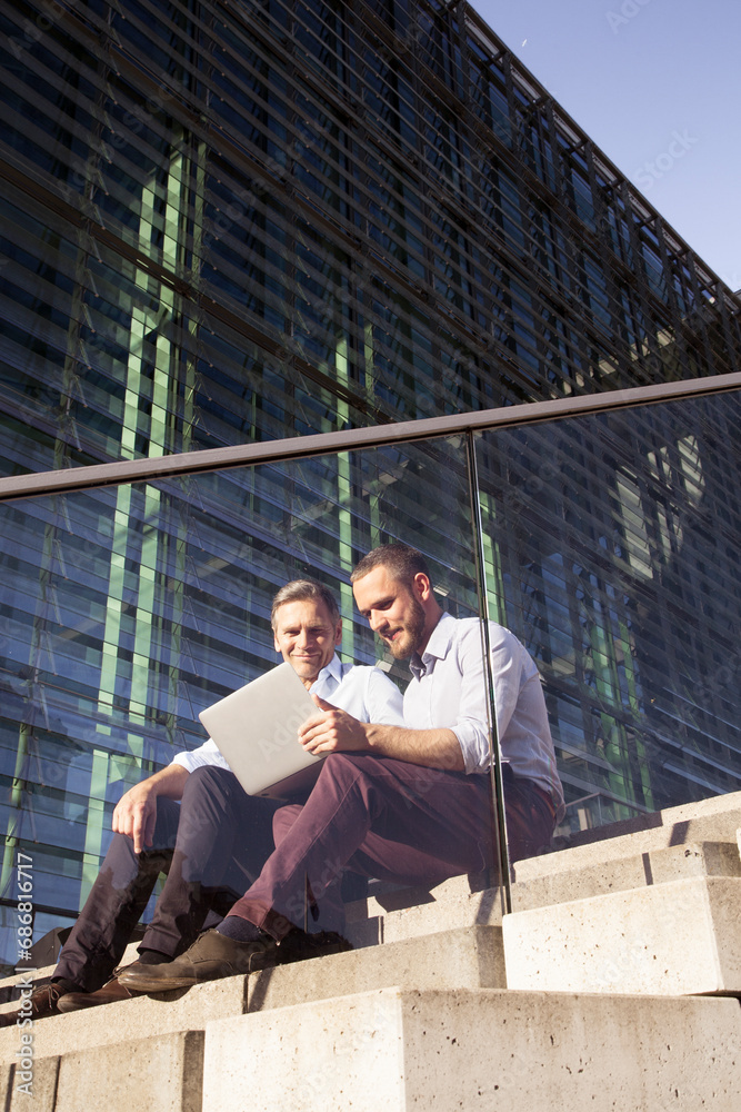 Two smiling businessmen sitting on stairs using laptop Two smiling businessmen sitting on stairs using laptop