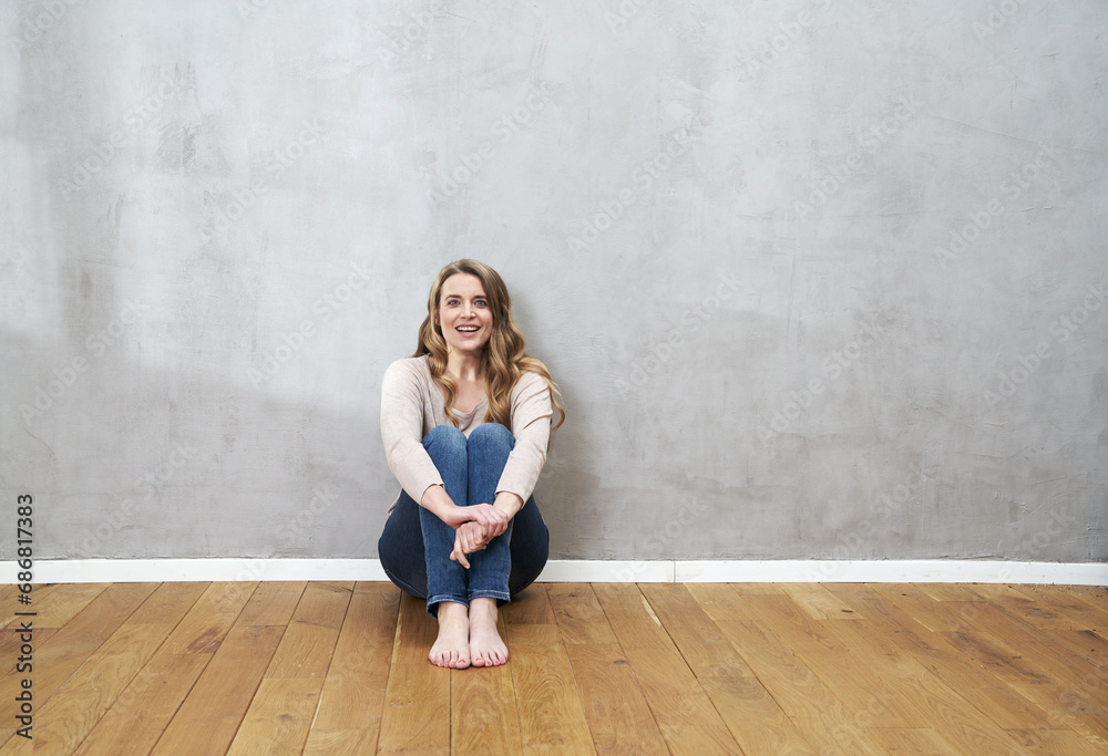 Smiling blond woman sitting on the floor in front of grey wall
