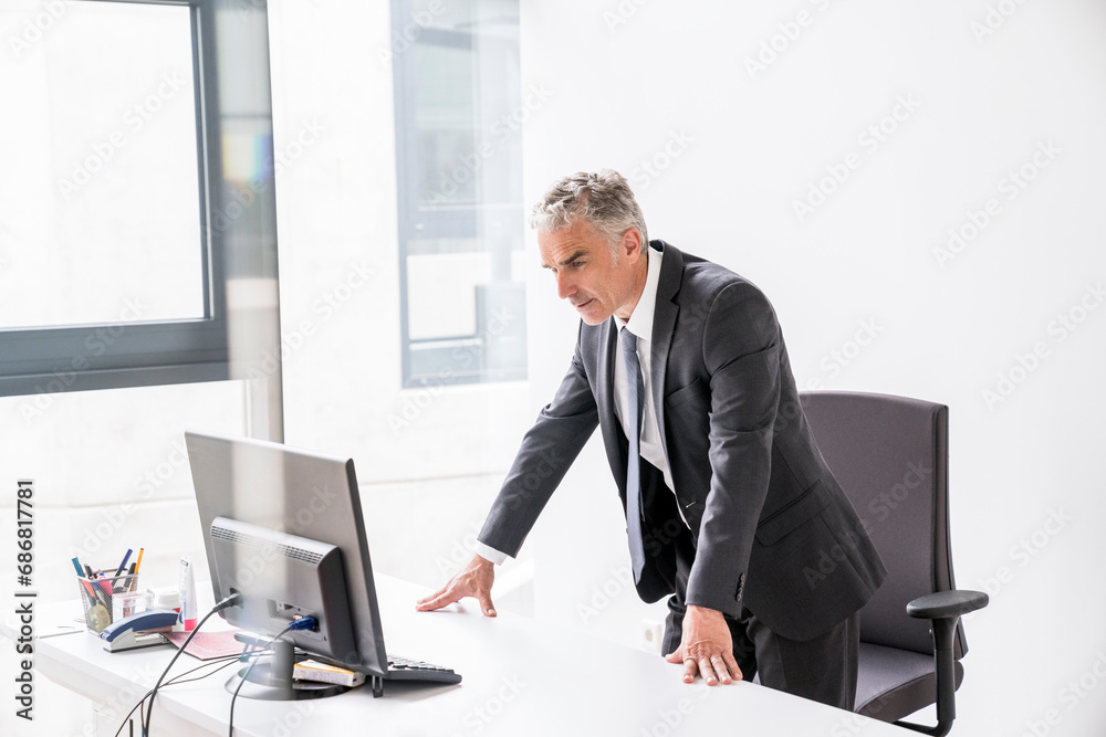 Mature businessman standing in office, looking at computer