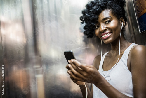 Portrait of happy woman with cell phone and earphones in underground train