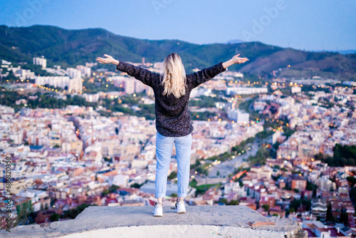 Rear view of carefree young woman standing above the city at sunrise, Barcelona, Spain