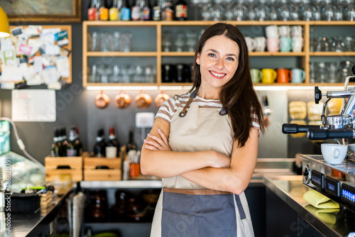 Happy female owner standing arms crossed in coffee shop