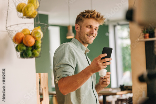 Young business owner drinking coffee, checking smartphone