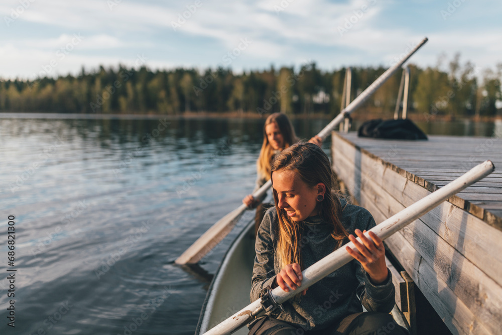 Two young women boating on lake - obrazy, fototapety, plakaty 