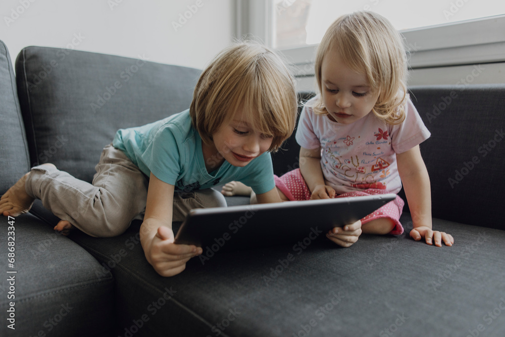 Brother and little sister using digital tablet on the couch at home Brother and little sister using digital tablet on the couch at home