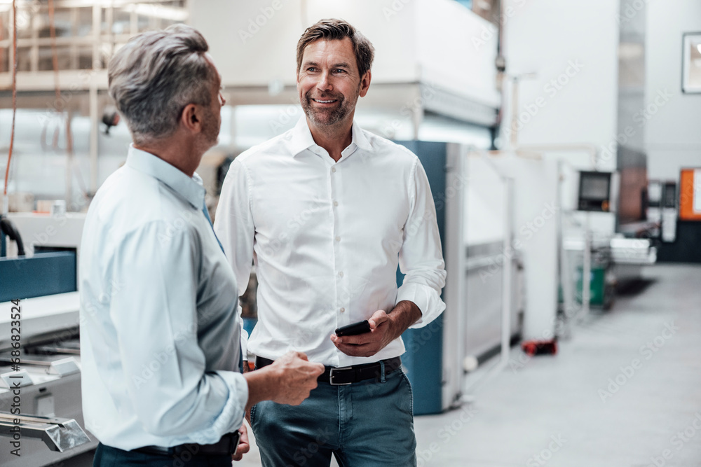Mature businessman holding smart phone while discussing with colleague in industry