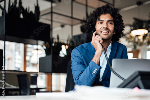 Smiling businessman talking on telephone while sitting with laptop at office