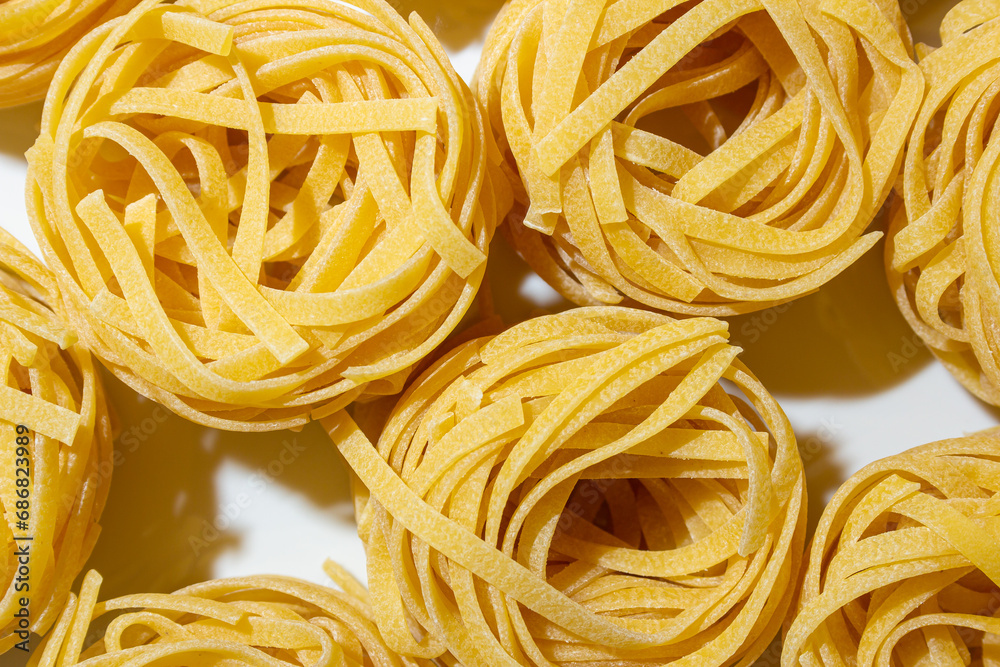 Uncooked Egg-Based Fettuccine Pasta: A Culinary Canvas of Ribbon-Shaped Macaroni, Creating a Lively and Textured Background for Gourmet Cooking. Dry Pasta. Raw Macaroni - Top View, Flat Lay Uncooked Egg-Based Fettuccine Pasta: A Culinary Canvas of Ribbon-Shaped Macaroni, Creating a Lively and Textured Background for Gourmet Cooking. Dry Pasta. Raw Macaroni - Top View, Flat Lay