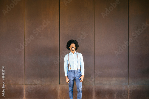 Portrait of smiling man wearing suspenders standing in front of rusty background © tunedin
