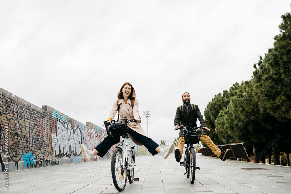 Carefree couple riding e-bikes on a promenade - obrazy, fototapety, plakaty 