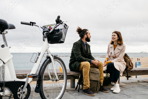 Couple sitting on a bench at beach promenade next to e-bike talking