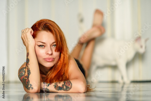 Portrait of red-haired tattooed woman in lingerie lying on the floor