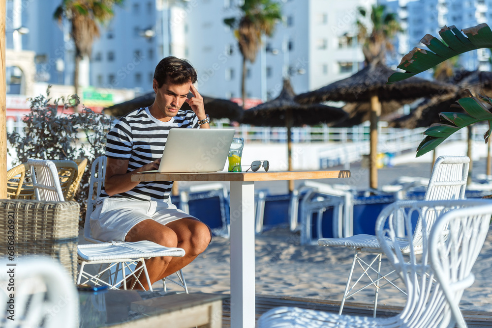 Man with laptop sitting on the terrace of a beach bar
