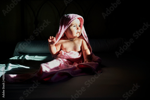 Cute baby girl in towel looking away while sitting on bed at home