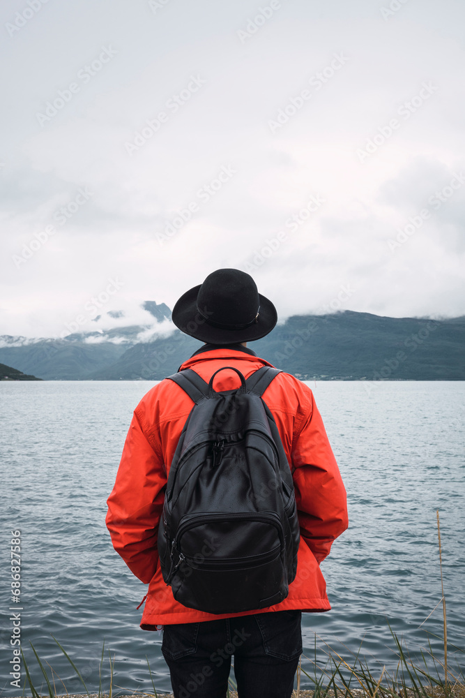Young man standing by water, looking at distance, rear view Young man standing by water, looking at distance, rear view