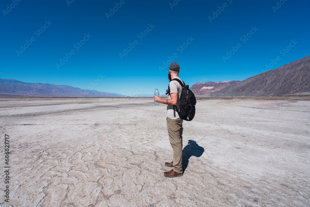 USA, California, Death Valley, man with backpack and water bottle standing in desert looking at distance USA, California, Death Valley, man with backpack and water bottle standing in desert looking at distance