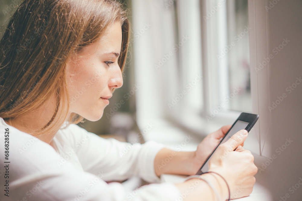 Young woman holding portable device at the window Young woman holding portable device at the window