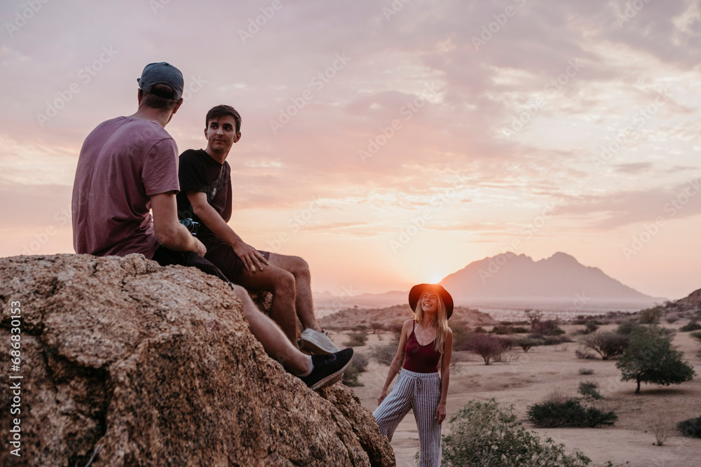 Namibia, Spitzkoppe, friends sitting on a rock at sunset