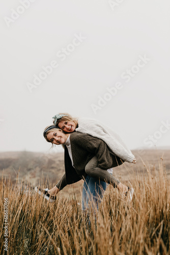 UK, Scotland, Isle of Skye, happy woman carrying friend piggyback in rural landscape photo