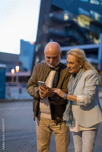 Spain, Barcelona, senior couple sharing cell phone in the city at dusk