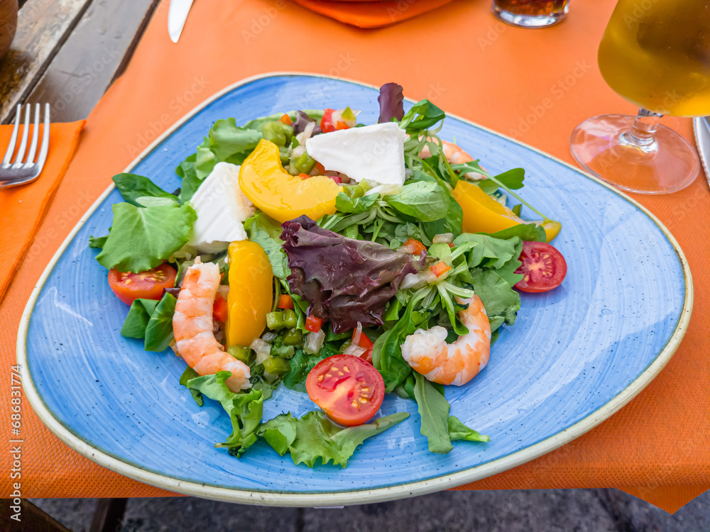 Salad with shrimp, tomatoes and feta cheese is on a plate in a restaurant