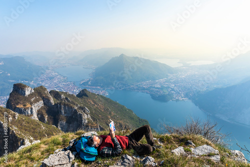 Rear view of hiker reading a book on mountaintop, Orobie Alps, Lecco, Italy