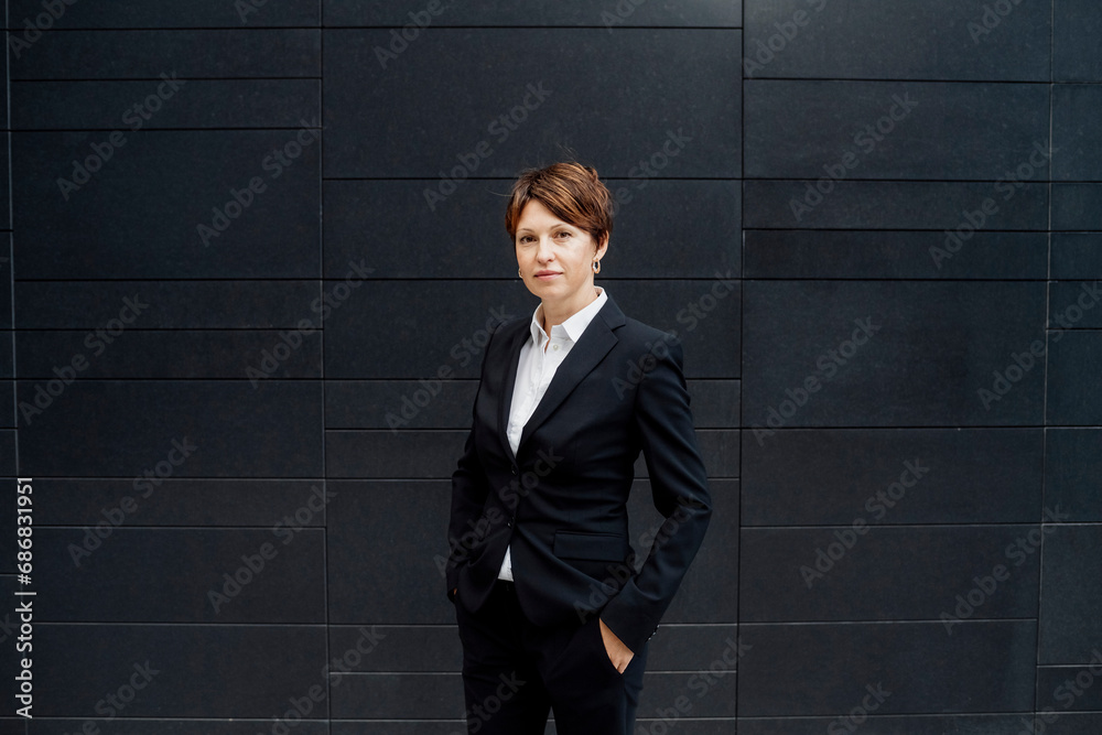 Confident female professional with hands in pockets standing against modern building Confident female professional with hands in pockets standing against modern building