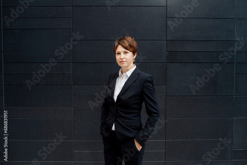 Confident female professional with hands in pockets standing against modern building