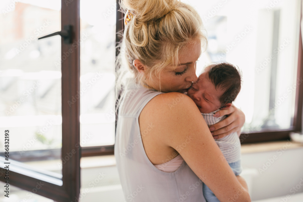 Mother holding her crying baby close to her shoulder at home Mother holding her crying baby close to her shoulder at home