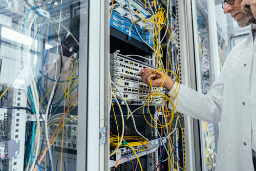 Mature man plugging in transceiver on fiber optic cable in data center photo