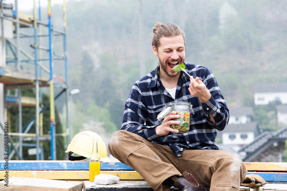 Construction worker eating salad while sitting outdoors at construction site