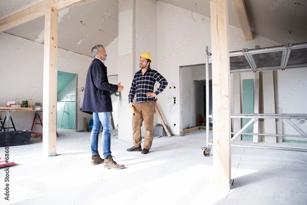 Architect and construction worker discussing while standing in renovating house
