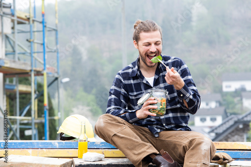 Construction worker eating salad while sitting outdoors at construction site photo