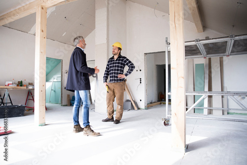 Architect and construction worker discussing while standing in renovating house photo
