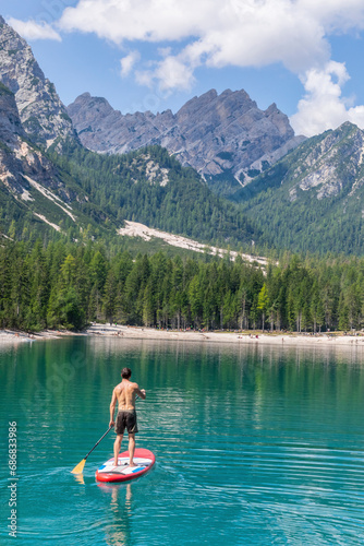 Male tourist paddleboarding on turquoise Pragser Wildsee, Dolomites, Alto Adige, Italy