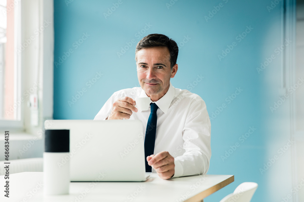 Portrait of confident businessman using laptop on table in office Portrait of confident businessman using laptop on table in office