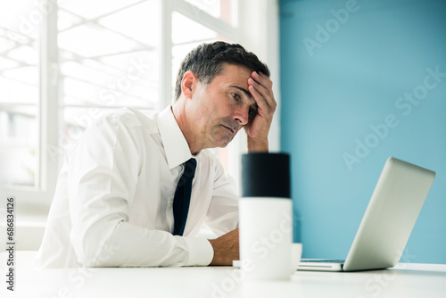 Serious businessman looking at laptop on table in office