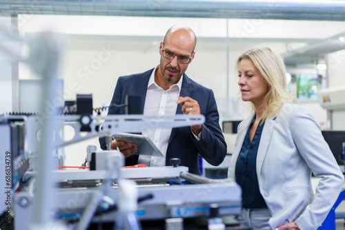 Confident businessman and businesswoman discussing while looking at machinery in factory photo