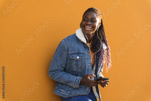 Teenage girl with mobile phone laughing while listening music against yellow wall photo