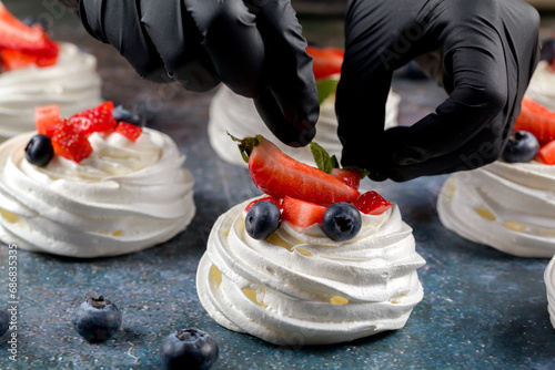 The process of making Pavlova dessert. Decorating the Pavlova dessert with fresh slices of strawberries, blueberries and mint leaves