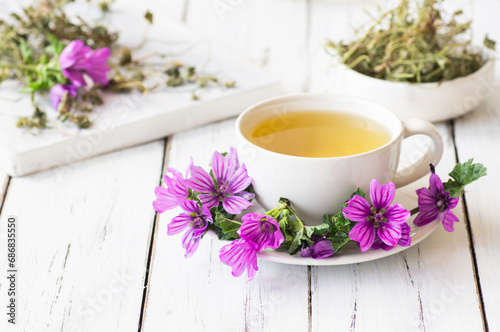 Cup of common mallow tea with fresh blooming malva sylvestris plant on white rustic table, alternative medicine photo