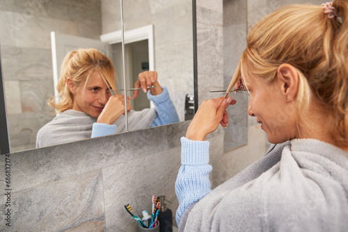 Mature woman looking in mirror cutting her own hair at home