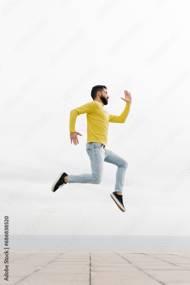 Carefree young man jumping on footpath against white wall