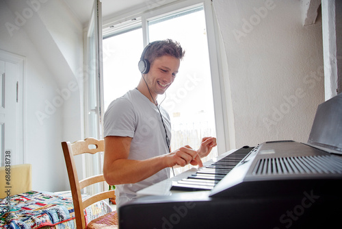 Smiling young man at home wearing headphones playing digital piano photo