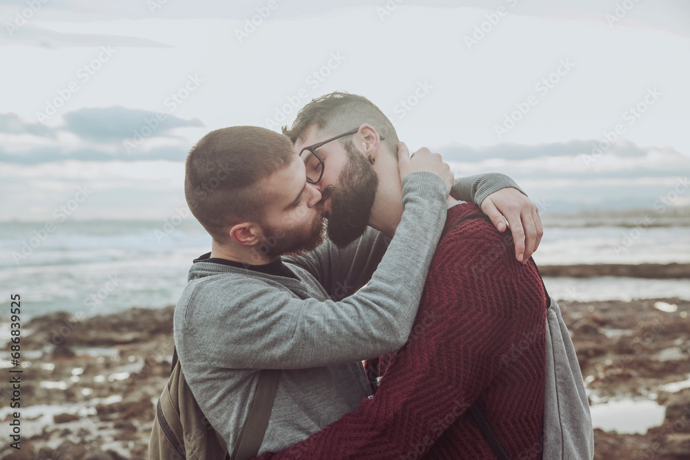 Young gay couple hugging and kissing in front of the sea