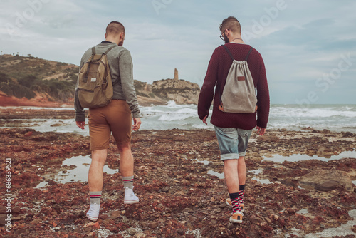 Spain, Oropesa del Mar, two young men walking on stony beach photo