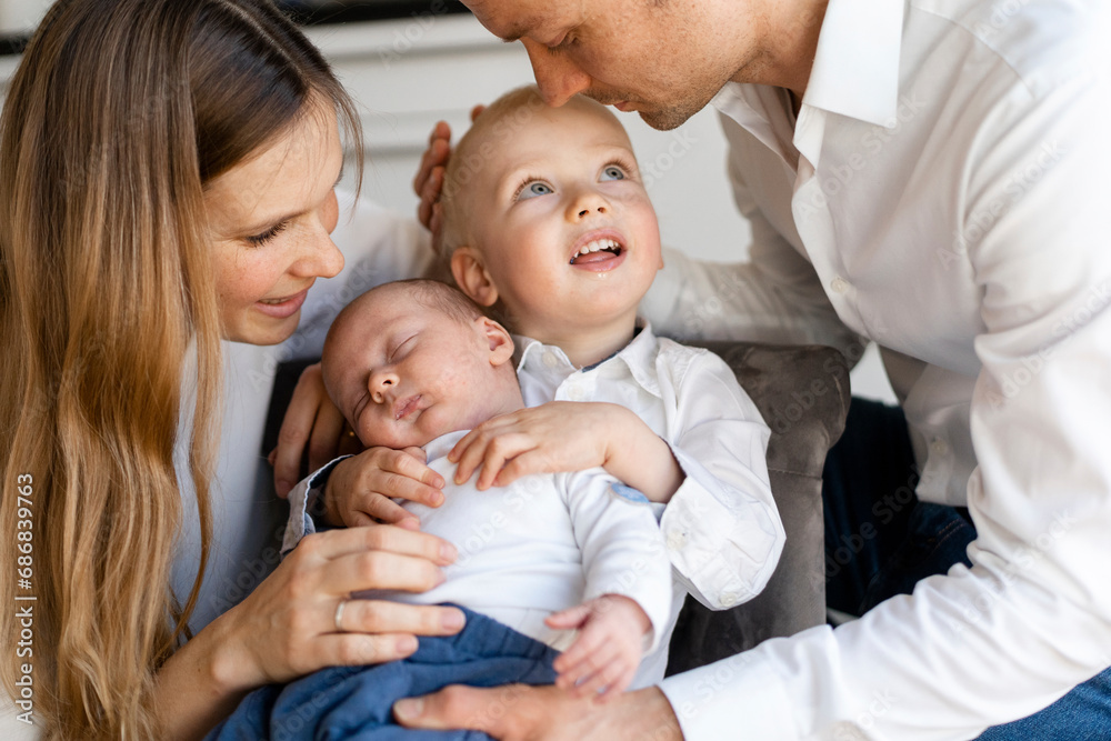 Mother and father taking care of baby boys sitting on chair at home