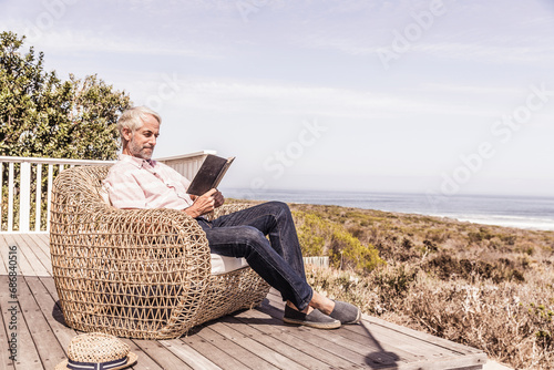 Obraz na płótnie Man reading a book on a deck at the coast w salonie