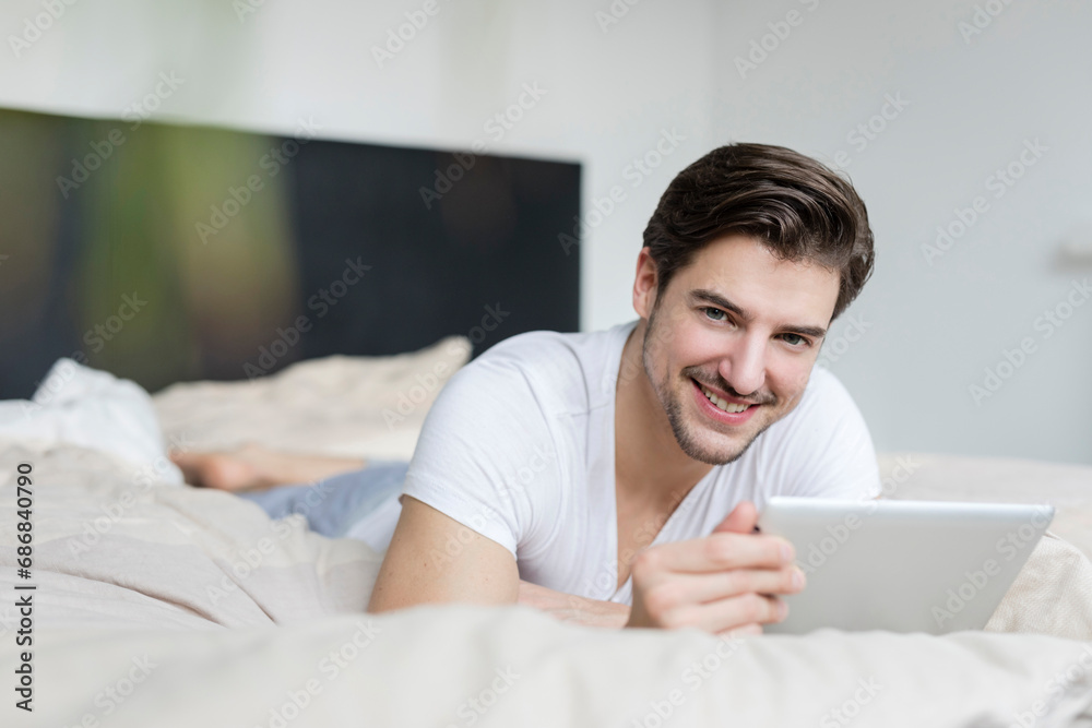 Portrait of smiling man lying on bed using tablet Portrait of smiling man lying on bed using tablet