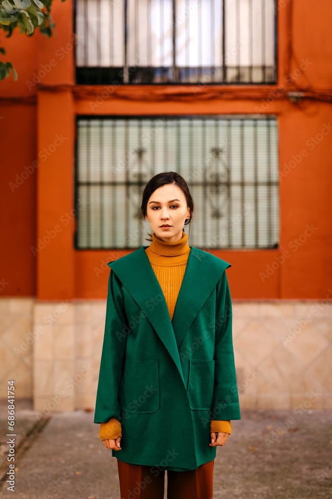 Fototapeta premium Young woman wearing green jacket standing against building in city